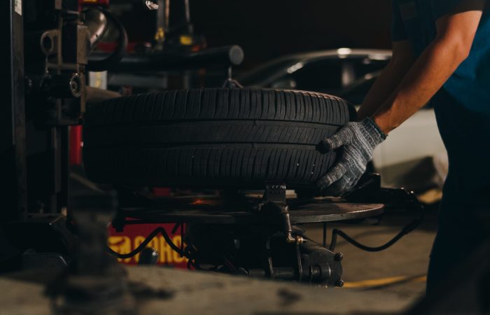 Professional car mechanic changing a car tire on lifted automobile at repair service station. Wheel alignment work at workshop night. Skillful Asian guy in uniform fixing car. Car service repair.